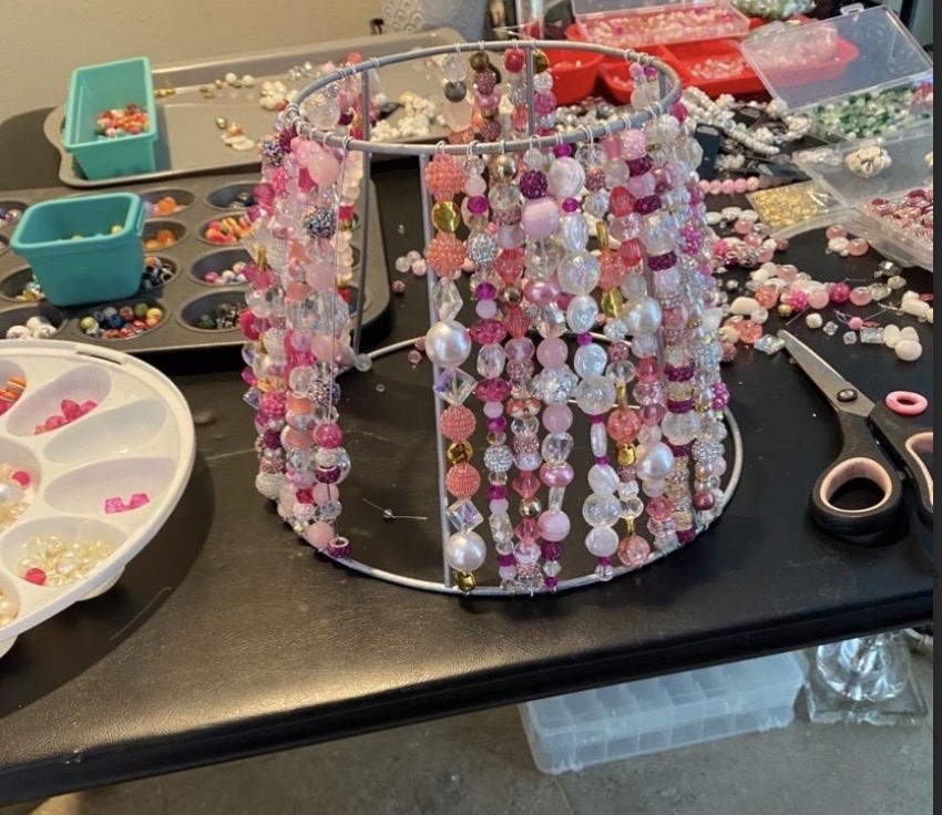 Pink beaded shade taking shape amid beads and tools on The Beaded Light worktable